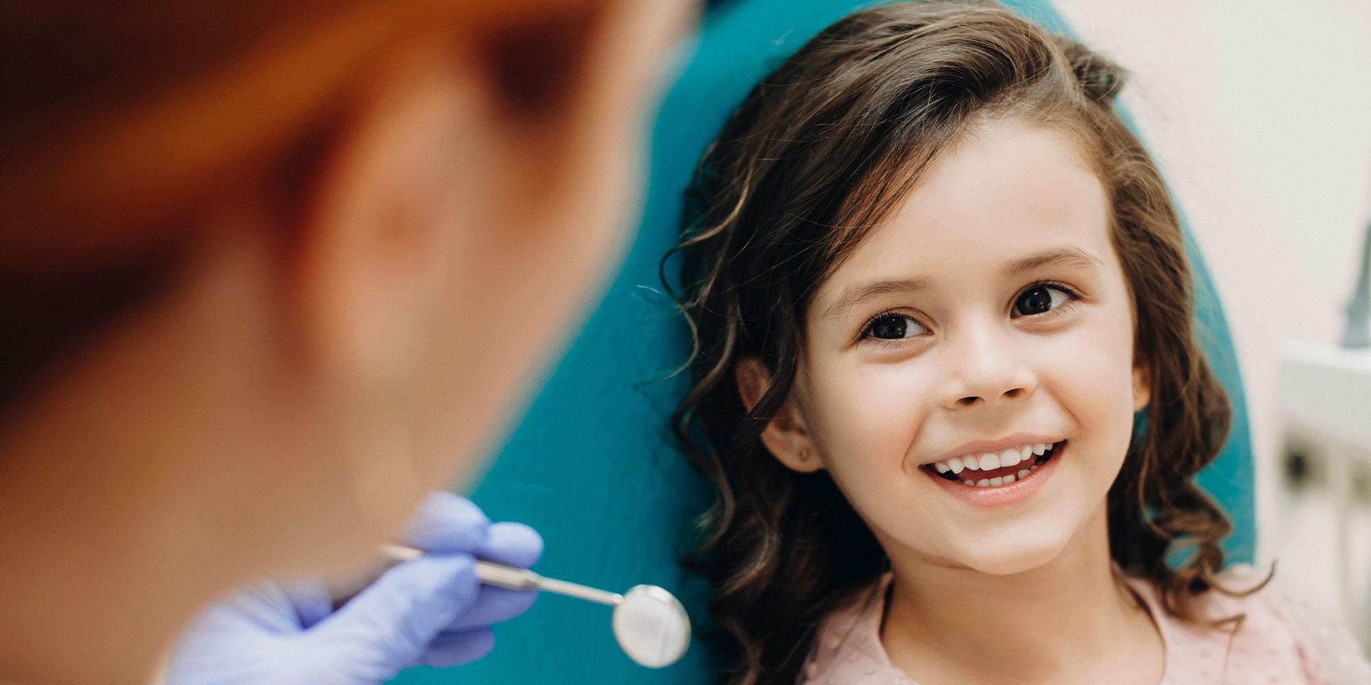 Lovely little kid smiling while talking with the pediatric dentist after doing a tenth examination in a pediatric